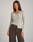 Cardigan donna beige con fiore e bottoni asimmetrici, indossato da Polly 4 con pantaloni spigati – vista tre quarti