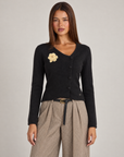 Cardigan donna nero con fiore e bottoni asimmetrici, indossato da Polly 4 con pantaloni spigati – vista frontale