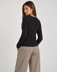 Cardigan donna nero con fiore e bottoni asimmetrici, indossato da Polly 4 con pantaloni spigati – vista posteriore