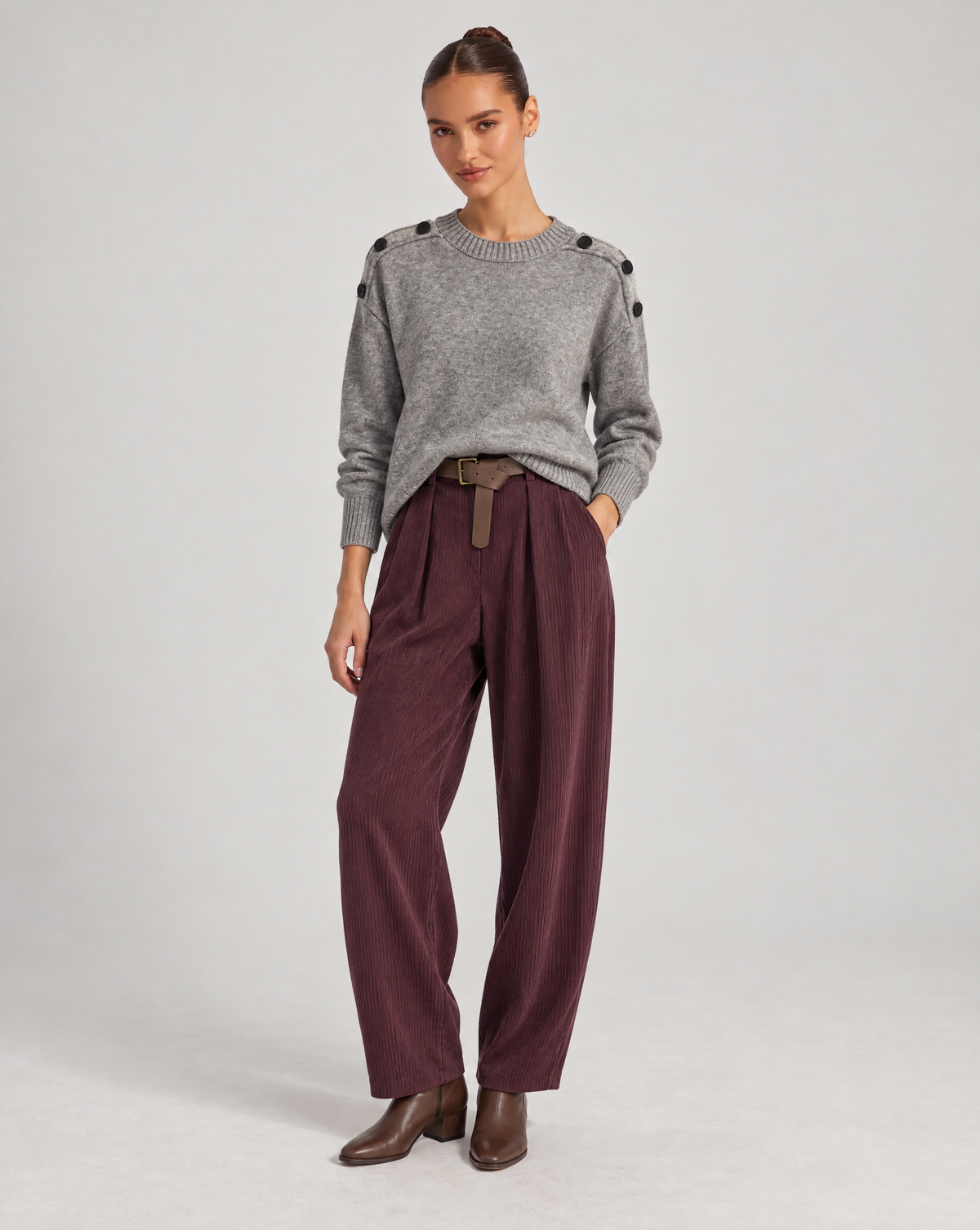 Polly 6 a corpo intero con maglia grigia con bottoni sulle spalle e pantaloni bordeaux a coste con cintura